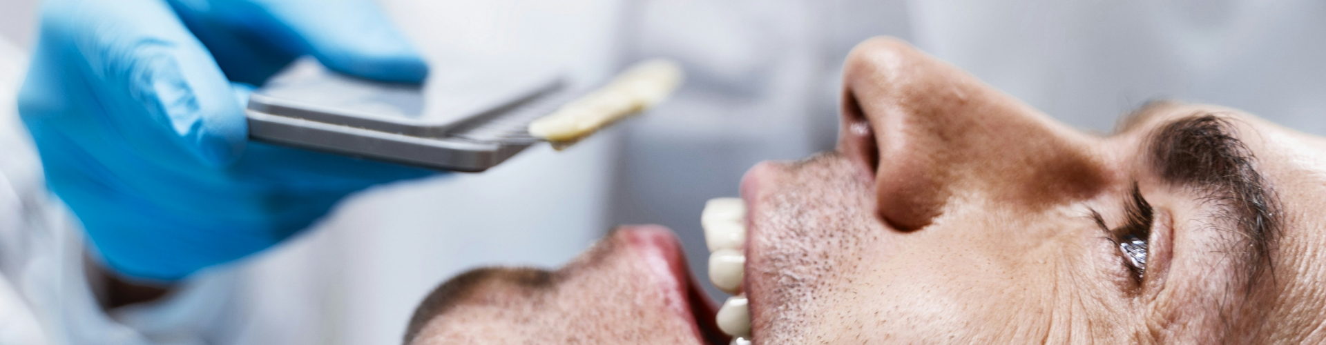 Gloved hand holding tooth shade-matching tool against man's smile.
